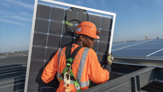 Construction worker in protective clothing carrying a solar panel