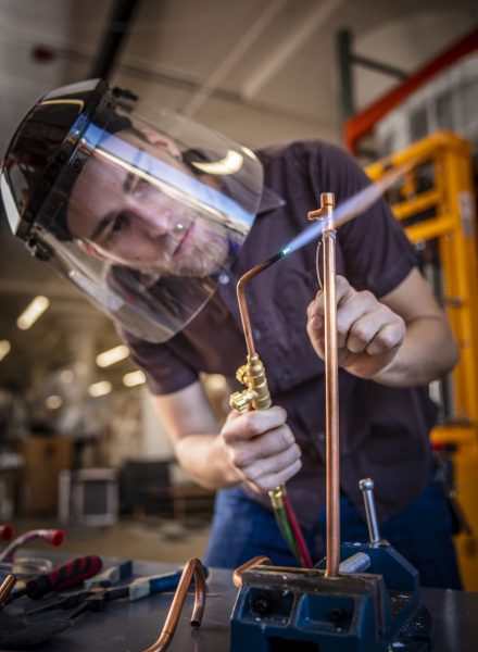 Man soldering copper pipes with a blow torch and wearing protective clothing