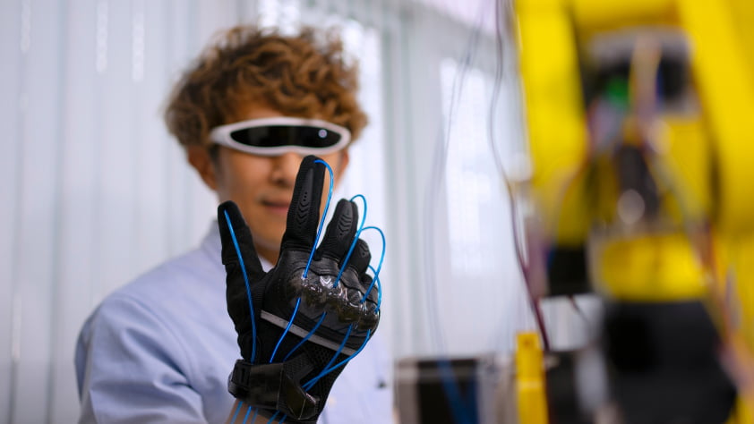 A researcher with smart glasses tests a robotic glove interface in a modern lab setup