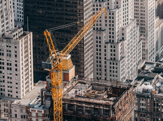 Urban construction scene featuring a yellow crane and a partially built high-rise among city towers.