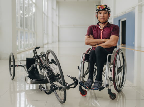 Framed by a modern, light-filled corridor, a wheelchair user in cycling gear poses confidently next to a high-performance handcycle, radiating strength and focus