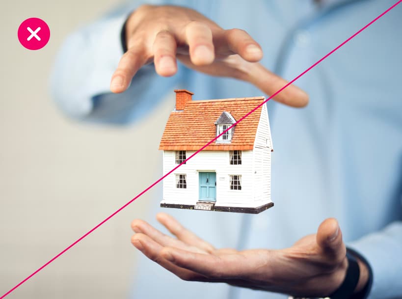 A person in a blue shirt holds their hands around a miniature house, appearing to levitate it in mid-air. The image appears overly staged or faked, and is marked with a red X.