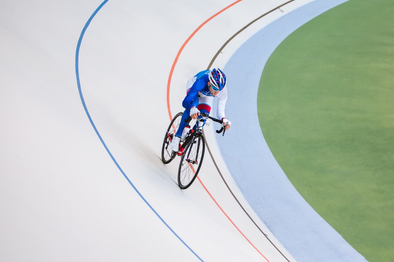 Cyclist leans into a turn on a velodrome, wearing a blue-white suit and helmet