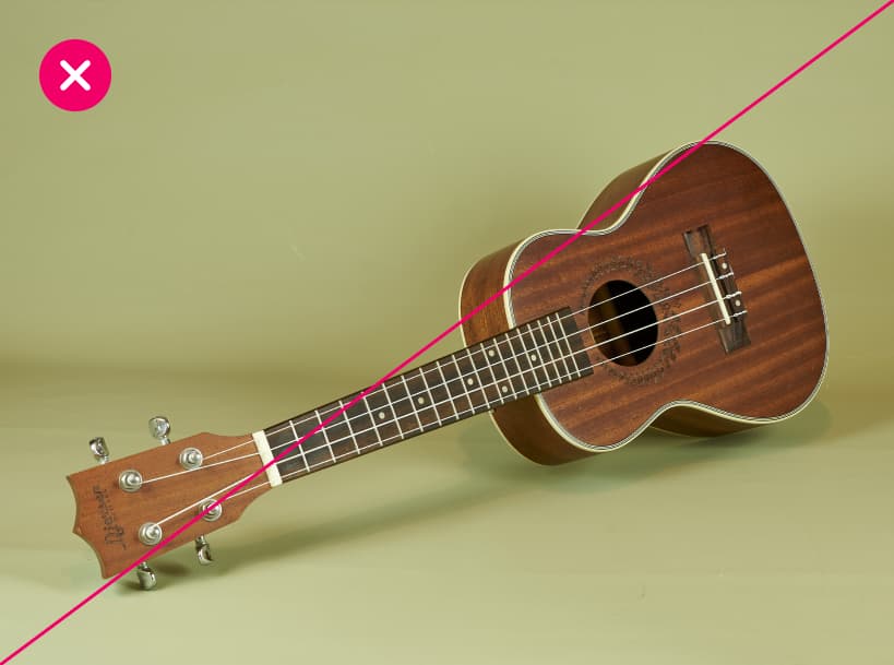 A handmade-looking acoustic guitar rests against a light-green background, implying that it has been made using Autodesk software. Marked with a red X.