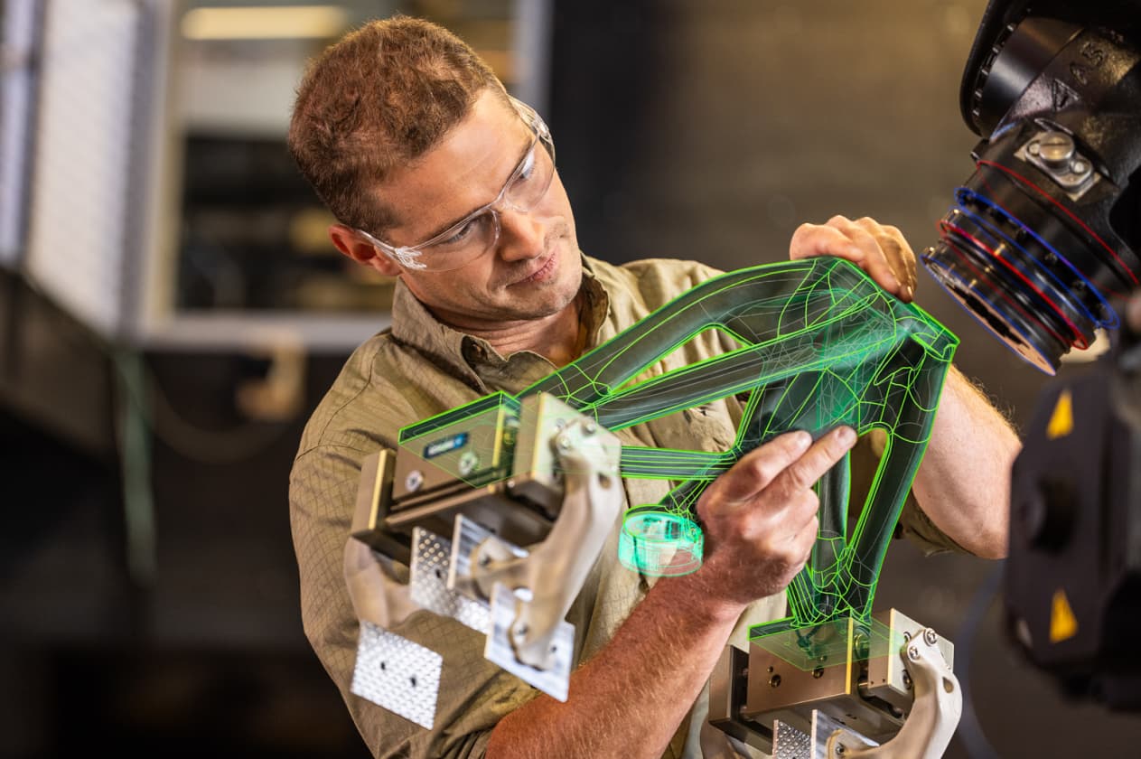 A mechanical engineer in safety glasses inspects a part, its surface structure digitally highlighted with bright green lines