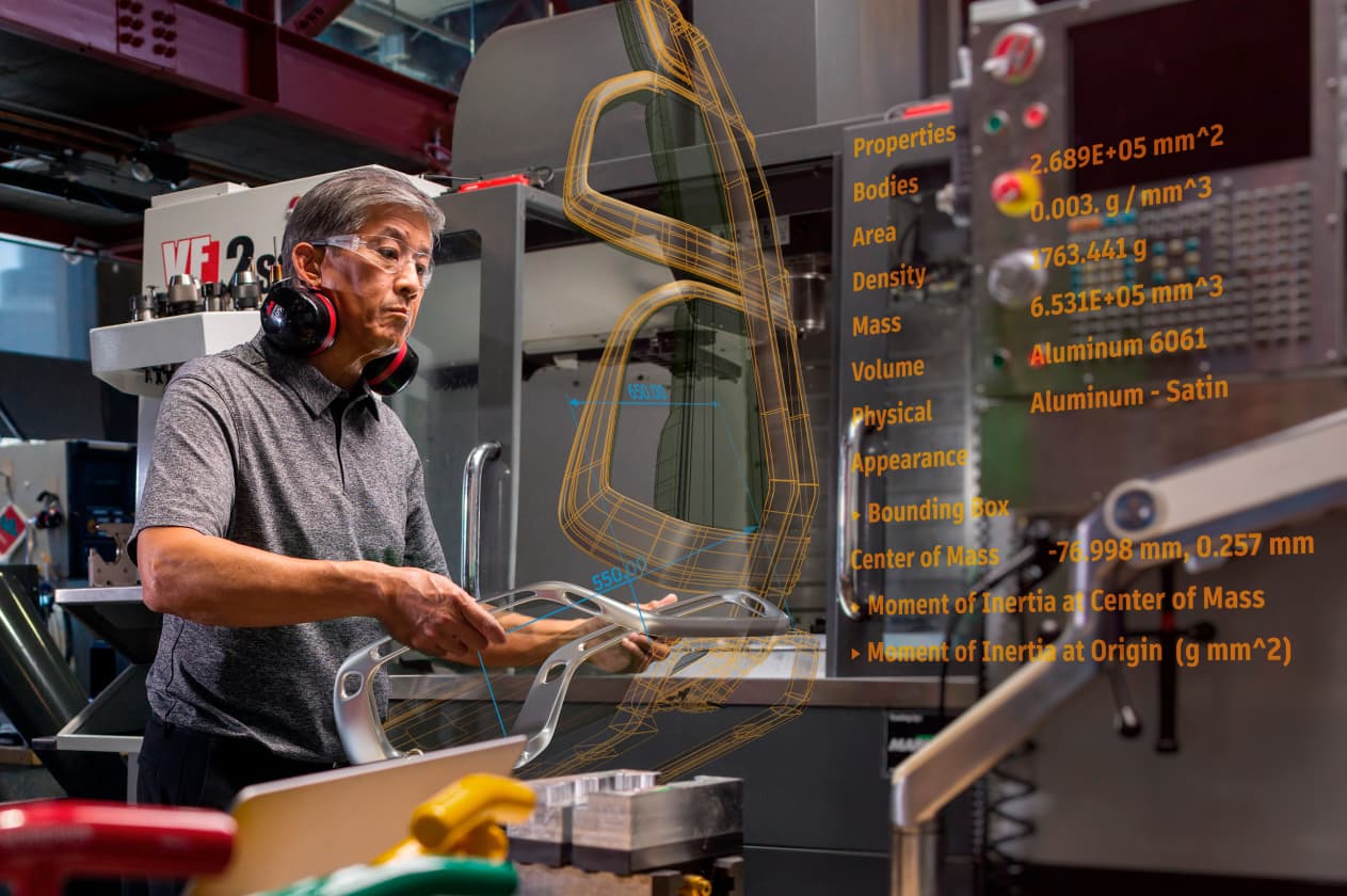 A technician wearing safety equipment inspects a cast metal part for a seat assembly. The rest of the assembly is digitally overlayed alongside information on the part's area, density, mass, and volume