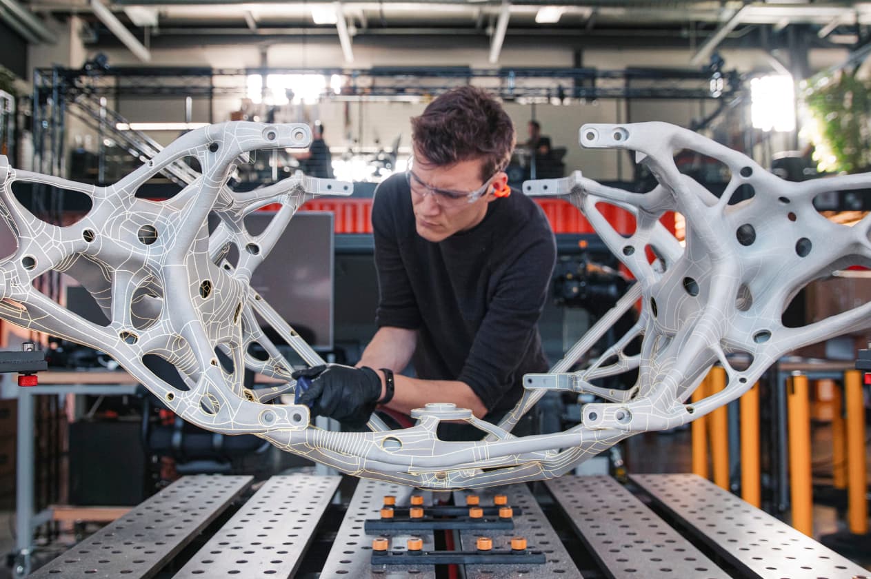 A worker inspects a large, complex, cast-molded assembly, its curvature digitally highlighted with subtle wireframe lines