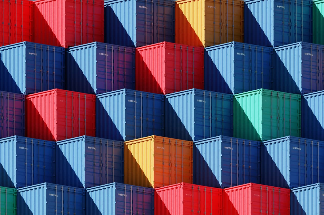 Abstract photo of a stack of brightly colored shipping containers, stacked neatly in a terraced formation, the sharp shadows cutting diagonally across the image
